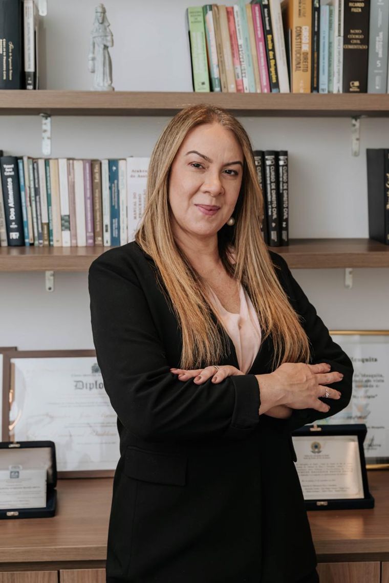 Sylvia Drummond em seu escritório, diante de estantes de livros jurídicos e diplomas